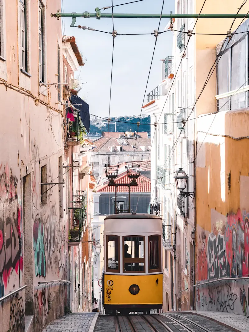 A yellow tram climbing a narrow Lisbon street between pastel houses