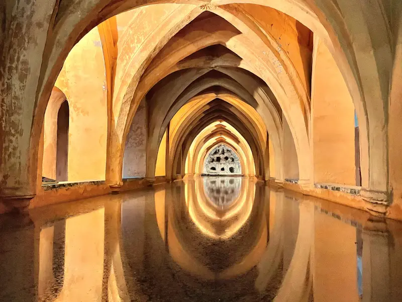 The vaulted Baths of María de Padilla reflected in still water
