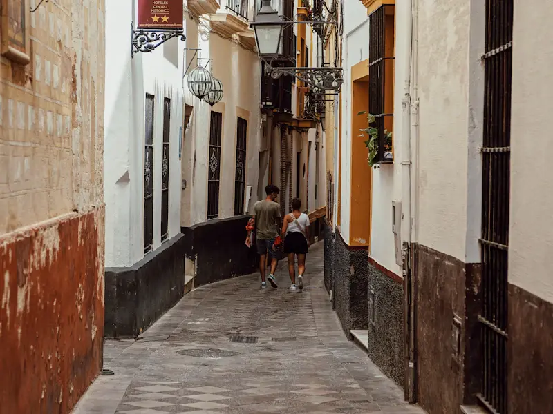 People walking down a narrow street between ochre and white houses