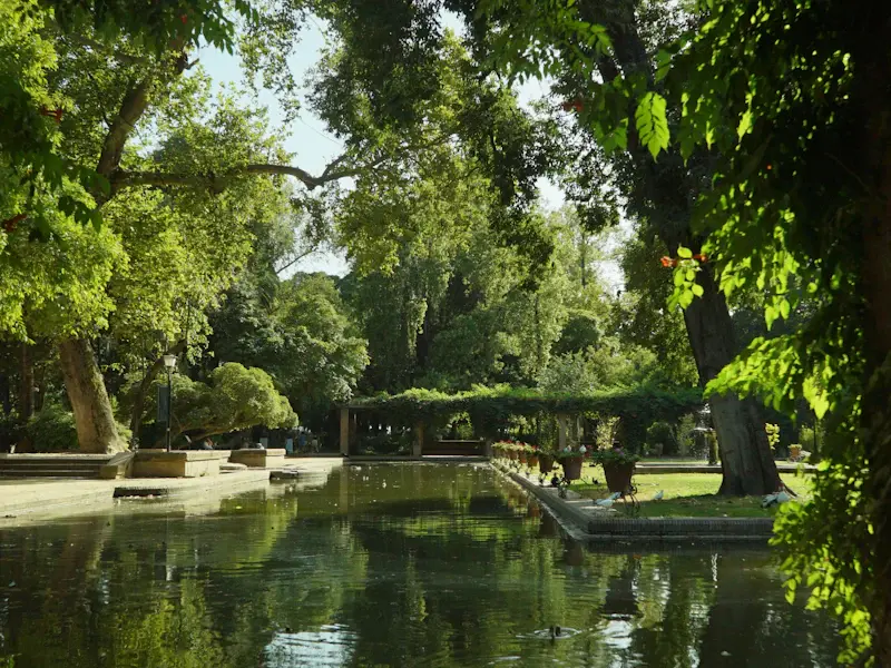 A pond reflecting trees, seen through an archway in the Parque de María Luisa